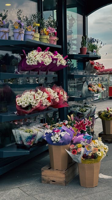 A display of vibrant floral arrangements and potted plants outside a flower shop, Hampstead Flowers, on a cloudy day. Several bouquets featuring white daisies, pink lilies, and purple asters are wrapp